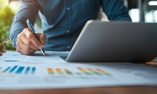 person drawing on a chart with a laptop in view